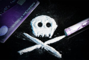 Georgia Drug Possession: Penalties and Defense Options - Marietta Attorneys Dean Phillips Law Office White powder arranged as a skull and crossbones beside a credit card and rolled banknote on a dark surface.